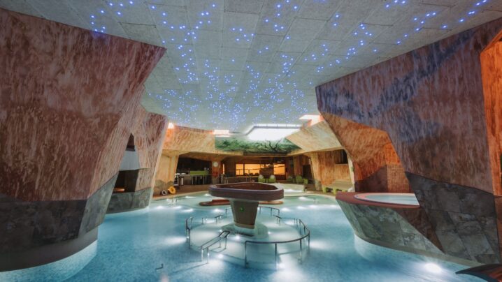 Large swimming pool with various water attractions. The starry sky characteristic of a water center can be seen on the ceiling.