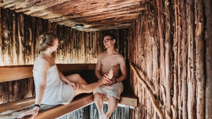 A young couple sitting opposite of each other in a juniper sauna.