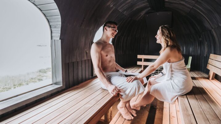 A young couple sitting opposite each other in the igloo sauna and holding each other.
