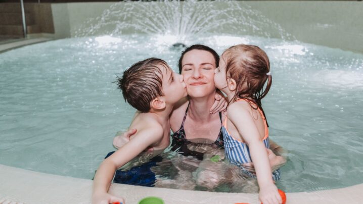 Mother and children in the pool. The children kiss their mother on the cheek.